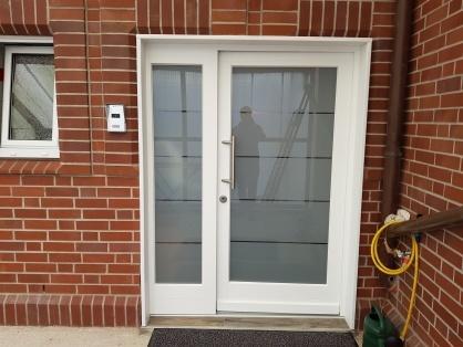 Weiße Haustür mit seitlichem Glaselement und Edelstahlgriff in roter Klinkerfassade, individuell gefertigt und passgenau eingebaut.