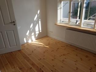 Massivholzboden im Wohnraum Heller Raum mit frisch verlegtem Massivholzboden aus Kiefer, weißen Wänden und großem Fenster für natürliches Licht.