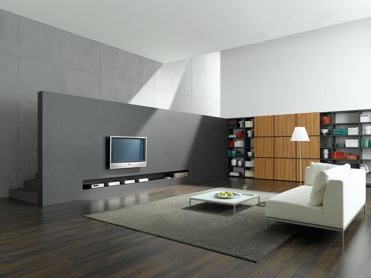 Offene Wohnraumimpression mit grauer TV-Trennwand zur Treppe und Einbauregal aus Holz und weißem Sofa